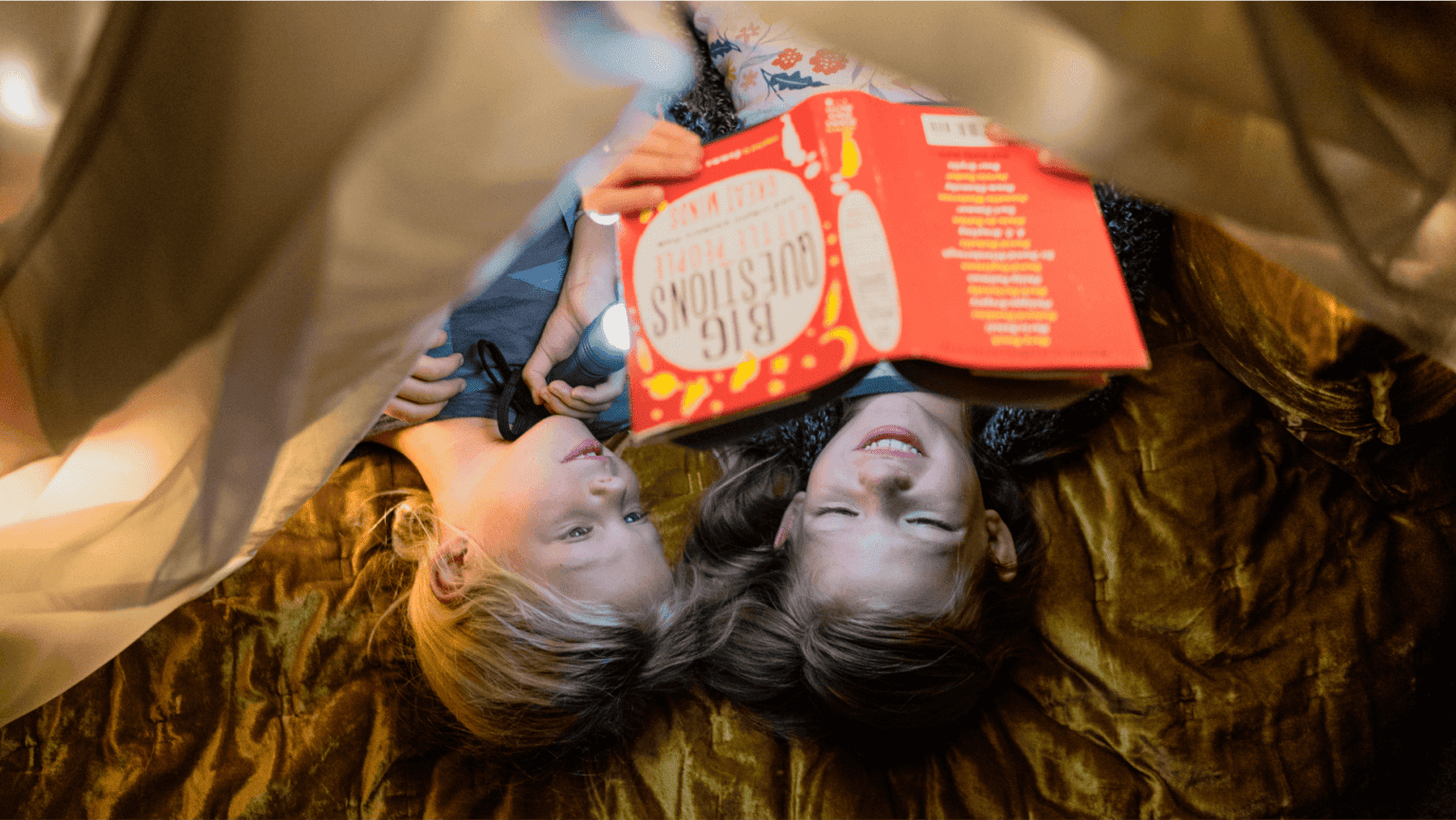 Looking down on, two kids read a nonfiction book in a blanket fort